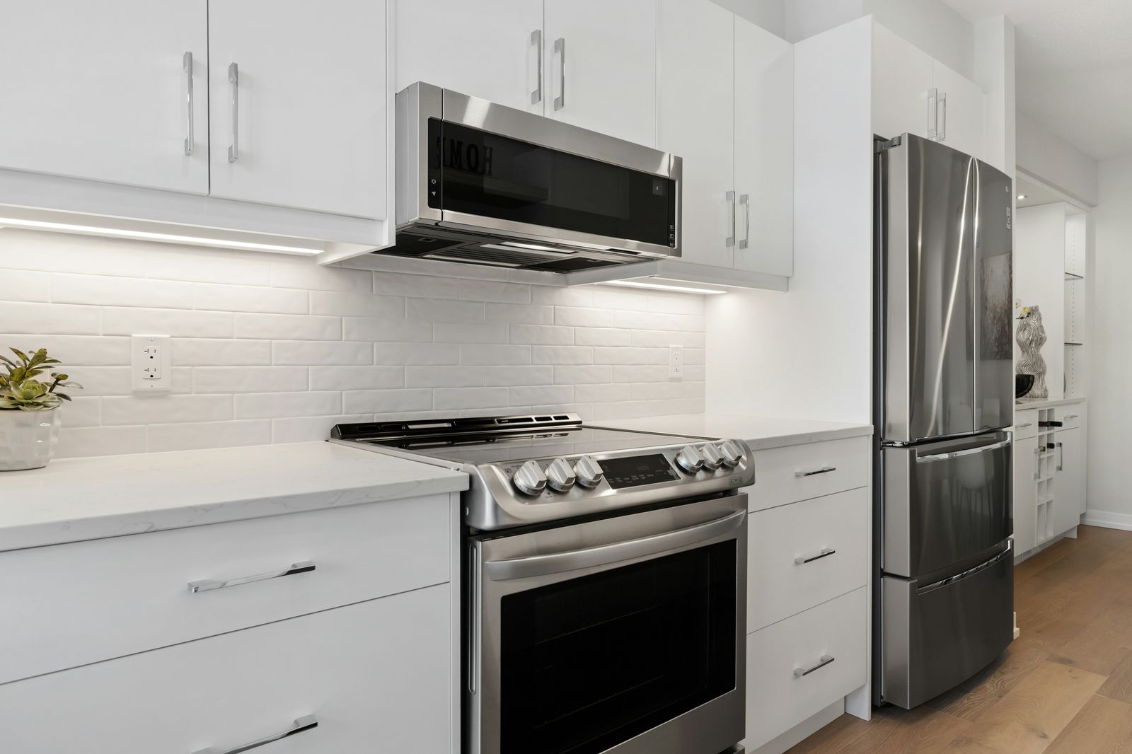 A white kitchen with a quartz countertop, a stainless steel stove, a microwave above it and a fridge.